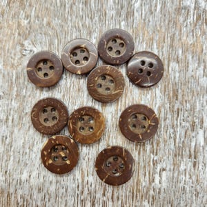 May include: Ten brown coconut shell buttons with four holes each. The buttons are arranged in a circle on a light brown wooden surface.
