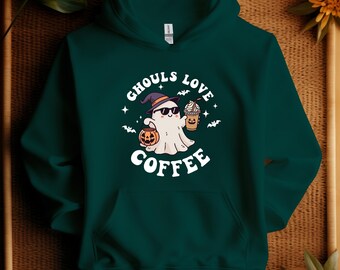 May include: Dark green hoodie with a front pocket and a drawstring hood. The front features a white graphic of a ghost wearing sunglasses and a witch hat, holding a pumpkin and a coffee drink. The text "Ghouls Love Coffee" is above and below the ghost.
