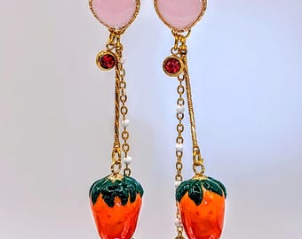 Peut inclure: Une paire de boucles d'oreilles pendantes avec un design de cœur superposé. Le cœur supérieur est rouge, le cœur du milieu est rose et le charme du bas est une fraise orange à feuilles vertes.