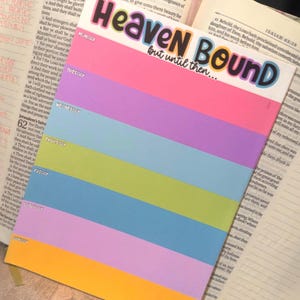 May include: A rectangular weekly planner notepad with the text "Heaven Bound but until then..." at the top. The notepad features seven horizontal color-blocked sections labeled Monday through Sunday in pink, purple, light blue, green, blue, violet, and orange.