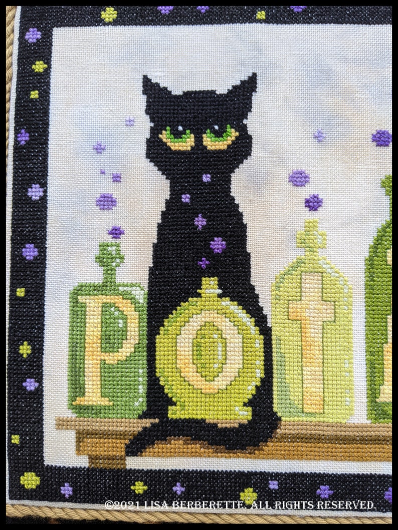 May include: Cross-stitch artwork featuring a black cat with green eyes, surrounded by green potion bottles. The word "POTION" is spelled out on the bottles. Purple star-shaped accents and a black border complete the design.
