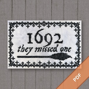 May include: Cross-stitch design with the text "1692 they missed one" in black on a white background. The design includes a black border and a broom graphic. The PDF file is displayed on a wooden surface.