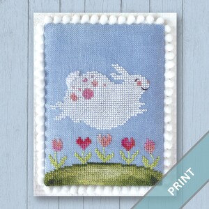 May include: Cross-stitch art featuring a white bunny with pink spots leaping over a green grassy area with pink and red heart-shaped flowers. The background is light blue, and the artwork is framed with white pom-poms. The word "PRINT" is visible.