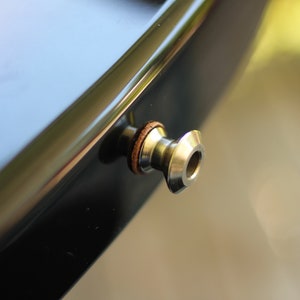 May include: Close-up of a black electric guitar with a gold-colored strap button.