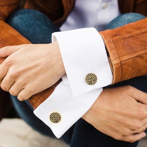 Op de afbeelding: Een paar gouden manchetknopen met een zwart en gouden luipaardprint.