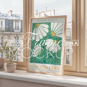 以下が含まれることがあります： 緑色の背景に、黄色い中心を持つ白い花が描かれた植物画のプリントが額装されています。プリントのタイトルは「フラワーマーケット」で、「ボタニカルアーカイブ」コレクションの一部です。フレームは木製の素材で、窓際に置かれています。