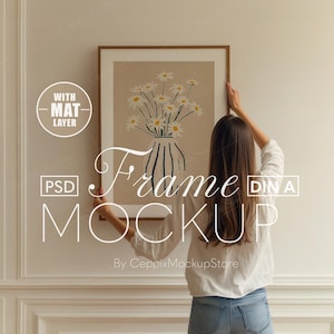 May include: A woman hangs a framed print of a floral illustration on a white wall. The print features a vase of white daisies with a brown background. The frame is brown wood with a white mount. The text "Frame Mockup" is written in white on the wall.