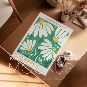 Puede incluir: Maqueta de póster con un diseño floral de grandes margaritas blancas y hojas verdes. El póster dice "Flower Market London". La maqueta está sobre una mesa de madera con objetos decorativos.