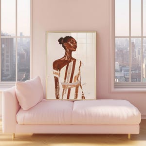 May include: A framed art print featuring a portrait of a person in a white and brown striped garment. The artwork is displayed on a pink chaise lounge in a room with large windows overlooking a cityscape. The frame is gold.