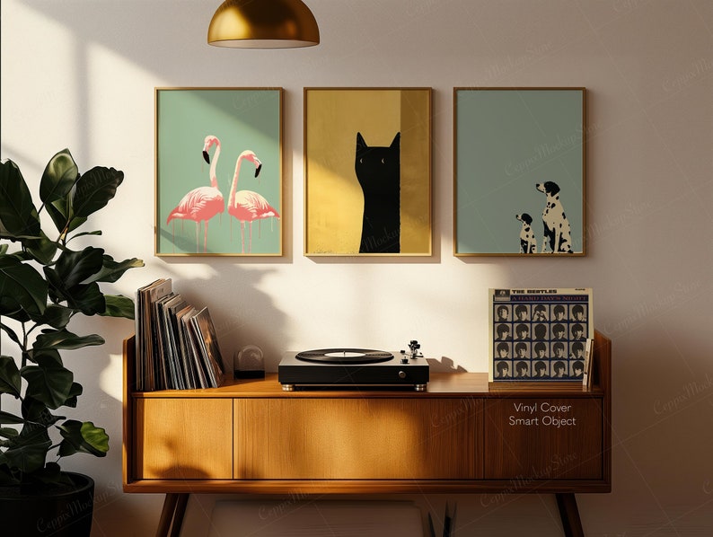 May include: Three framed art prints with gold frames. The prints feature a pair of pink flamingos, a black cat, and a Dalmatian dog with a puppy. A record player and vinyl records sit on a wooden cabinet. A Beatles album cover is visible.