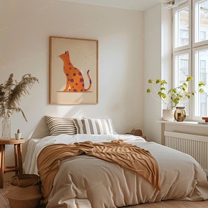 May include: A bedroom scene featuring a bed with neutral-toned bedding and a brown throw blanket. A framed artwork of an orange cat with purple spots hangs above the bed. The room is decorated with a wooden stool, a vase of dried plants, and a window with natural light.