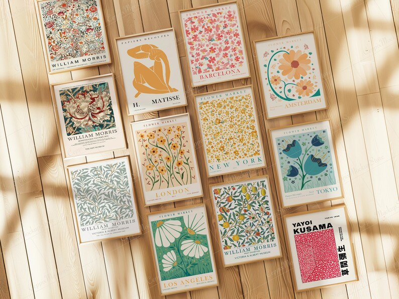 May include: A collection of framed art prints featuring floral designs, botanical patterns, and abstract art. The prints include text such as "William Morris", "Matisse", and "Flower Market" with city names. The frames are a light brown color, and the background is a wooden surface.