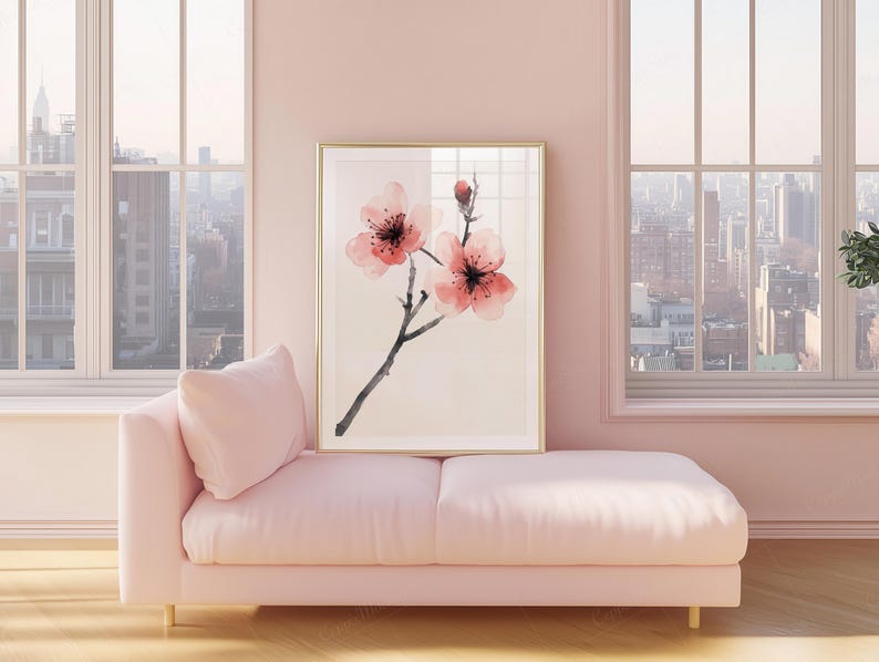 May include: A framed floral art print featuring pink cherry blossoms with black stems and a gold frame. The artwork is displayed above a pink chaise lounge with a matching pillow, set against a pink wall and large windows.