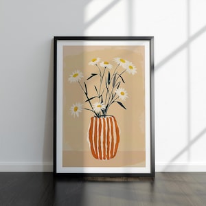 May include: Framed art print showing a vase of white daisies with green stems. The vase is orange with vertical white stripes. The background is a light tan colour. The frame is black and the artwork is leaning against a white wall.