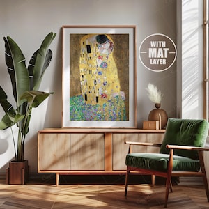 Op de afbeelding: Een ingelijste print van Gustav Klimts schilderij "De Kus". Het schilderij toont twee figuren in een gouden omhelzing, met een achtergrond van kleurrijke geometrische patronen.