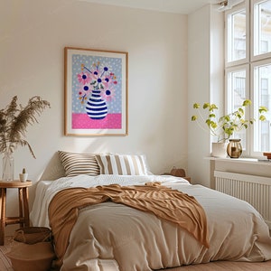 May include: A framed art print featuring a vase with blue and white stripes filled with pink and blue flowers. The artwork hangs above a bed with striped pillows and a brown blanket. The room has a neutral color palette with a window and a small wooden table.