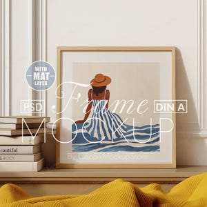 May include: A framed illustration of a woman in a blue and white striped dress and a brown hat, sitting on a beach. The frame is made of wood and has a light brown finish. The illustration is titled "Frame Mockup" and is by "CeppixMockupStore".