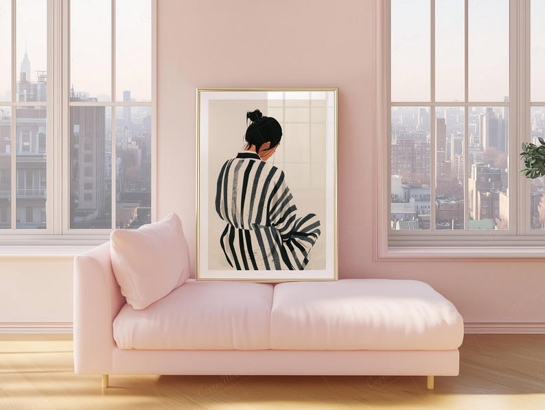 May include: A framed art print featuring a person in a black and white striped garment, seated with their back to the viewer. The artwork is displayed above a pink chaise lounge, set against a backdrop of large windows overlooking a cityscape.