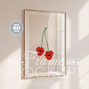 Puede incluir: Una maqueta de marco dorado con una capa de paspartú blanca, que presenta una ilustración simple de dos cerezas rojas con tallos verdes. El texto "Frame Mockup" está escrito en blanco en la parte inferior del marco. El texto "DIN A" está escrito en blanco en el lado derecho del marco. El texto "WITH MAT LAYER" está escrito en blanco en un círculo gris en la esquina superior izquierda de la imagen.