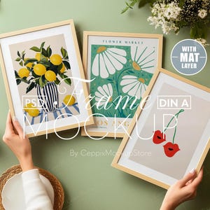 May include: Three framed prints with different designs. The first print features a vase of lemons with a blue and white striped pattern. The second print features a floral design with white daisies on a green background. The third print features a red cherry with a stem and leaves on a cream background. The text "FLOWER MARKET" is at the top of the second print. The text "WITH MAT LAYER" is in a white rectangle on a gray background. The text "DIN A" is in a white rectangle on a gray background.