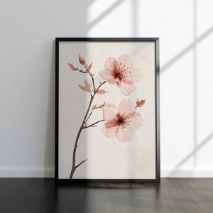 May include: A framed art print with a watercolour illustration of cherry blossoms. The artwork depicts delicate pink flowers with dark red centres and a brown stem against a cream background. The black frame adds a modern touch.