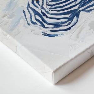 May include: An abstract painting on canvas with blue and white brushstrokes. The artwork has a textured appearance, with visible paint strokes and a white background. The canvas is stretched and mounted on a wooden frame. The painting is a close-up view.