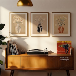 May include: Three framed art prints featuring vases with daisies, displayed above a wooden cabinet. The cabinet holds a record player, vinyl records, and a vintage album cover that reads "Pete Fountain". The art prints have gold frames and beige backgrounds.
