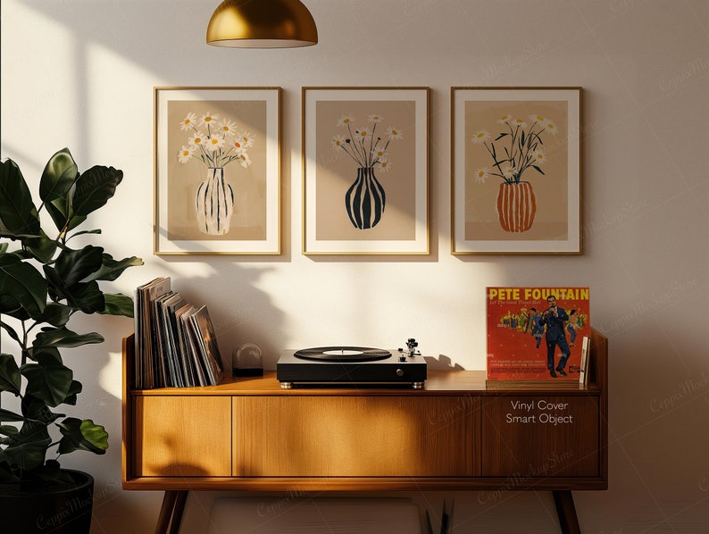 May include: Three framed art prints featuring vases with daisies, displayed above a wooden cabinet. The cabinet holds a record player, vinyl records, and a vintage album cover that reads "Pete Fountain". The art prints have gold frames and beige backgrounds.