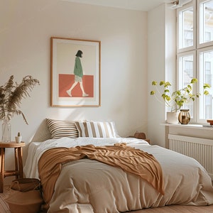 May include: A bedroom scene with a bed covered in a beige comforter and a brown throw blanket. Decorative pillows with stripes and a framed art print of a person walking are visible. A wooden side table with a vase and a woven basket add to the room's decor.