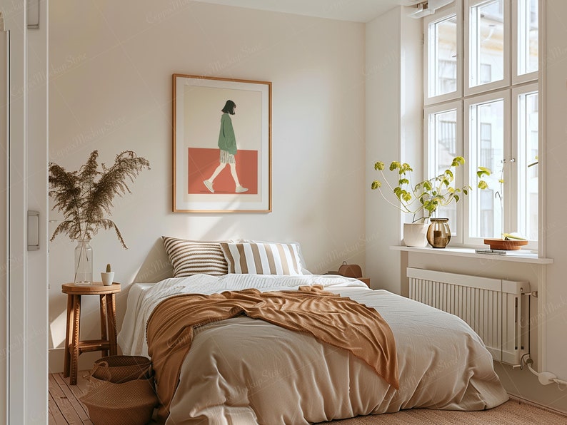 May include: A bedroom scene with a bed covered in a beige comforter and a brown throw blanket. Decorative pillows with stripes and a framed art print of a person walking are visible. A wooden side table with a vase and a woven basket add to the room's decor.