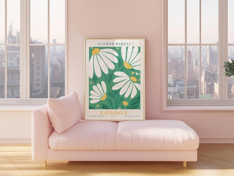 May include: A framed art print featuring a botanical illustration of white daisies with yellow centers on a green background. The print is labeled "LONDON FLOWER MARKET" and is displayed above a pink chaise lounge in a room with large windows.
