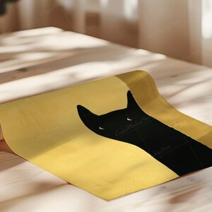 May include: A rolled-up poster featuring a black cat silhouette against a gold background. The cat's head and ears are visible, with a minimalist design. The poster is on a light-colored wooden surface.