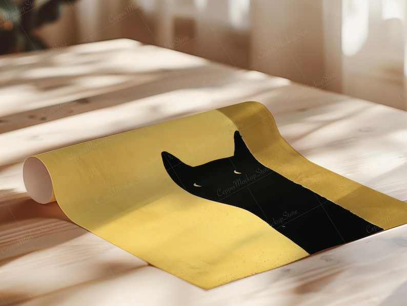 May include: A rolled-up poster featuring a black cat silhouette against a gold background. The cat's head and ears are visible, with a minimalist design. The poster is on a light-colored wooden surface.