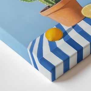 May include: A canvas art print showing a cactus in a terracotta pot, with lemons on a blue and white striped surface. The artwork has a bright, summery feel, with a light blue background.