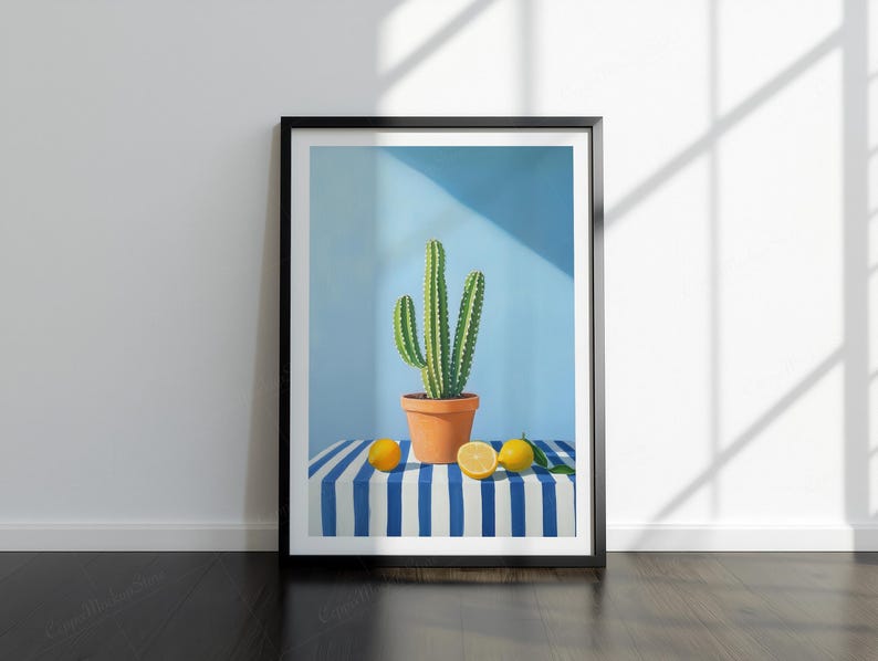 May include: Framed art print showing a cactus in a terracotta pot, set against a light blue backdrop. Lemons are placed on a blue and white striped surface. The artwork is in a black frame.