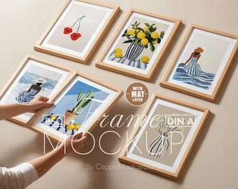 以下が含まれることがあります： 様々なイラストが描かれた額入りのアートプリントのコレクション。さくらんぼ、花瓶に入ったレモン、ストライプのドレスを着た女性、サボテン、デイジーなど。フレームは、白いマット付きの明るい木材です。