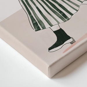 May include: Canvas art print showing a watercolor illustration of a person walking. The artwork depicts a green and white striped skirt, black sock, and a black and white shoe. The background is a light pink and beige.
