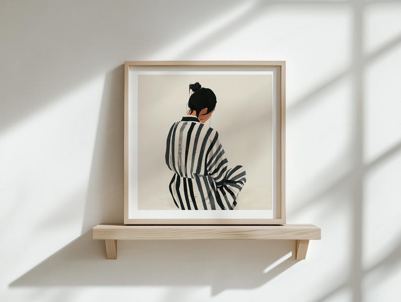 Puede incluir: Impresi&oacute;n art&iacute;stica enmarcada que muestra a una persona con una prenda a rayas, vista por la espalda. La obra de arte se exhibe en una estanter&iacute;a de madera clara contra una pared blanca. Las sombras de la luz natural se proyectan.
