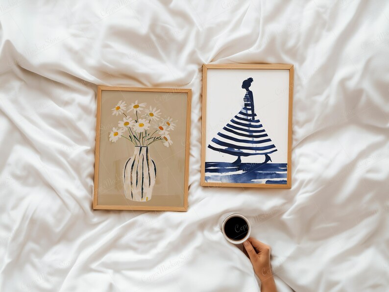 Puede incluir: Dos impresiones art&iacute;sticas enmarcadas sobre una superficie blanca. Una presenta un jarr&oacute;n con margaritas, la otra una figura con un vestido a rayas. Una mano sostiene una taza de caf&eacute;. El arte es de estilo minimalista y acuarela.