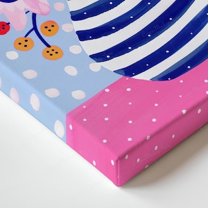 May include: A corner view of a canvas art piece. The artwork features a blue background with white polka dots, a pink section with white polka dots, and a blue and white striped design. Floral and berry elements are also visible.