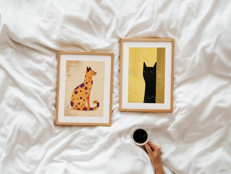 Puede incluir: Dos impresiones art&iacute;sticas enmarcadas con ilustraciones de gatos. Una muestra un gato naranja con manchas moradas sobre un fondo beige. La otra representa un gato negro sobre un fondo dorado. Ambas en marcos de madera.