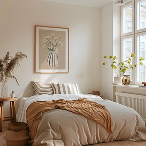 May include: A cozy bedroom scene featuring a bed with a tan blanket and pillows. A framed artwork of daisies in a vase hangs above the bed. A small wooden stool holds a glass vase with dried plants. A window with natural light.
