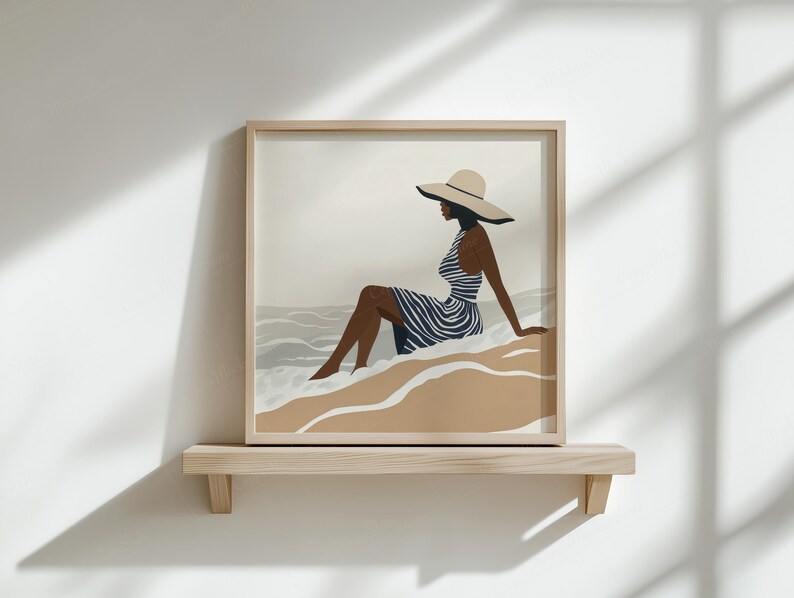 Puede incluir: Una impresi&oacute;n art&iacute;stica enmarcada representa a una persona con un vestido a rayas y un sombrero de ala ancha, sentada en una playa. La obra de arte presenta una paleta de colores neutros con tonos beige, azul y marr&oacute;n. La impresi&oacute;n se exhibe en una estanter&iacute;a de madera contra una pared blanca.
