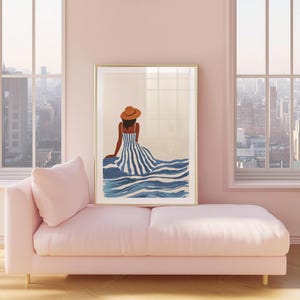 May include: A framed art print featuring a woman in a striped dress and hat, seated near blue water. The artwork has a gold frame and is displayed above a pink chaise lounge. The room has large windows with a city view.