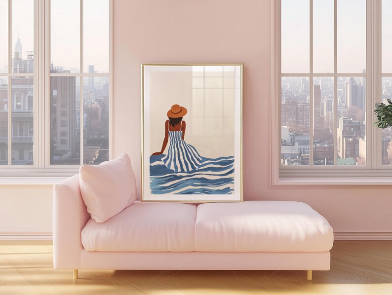 May include: A framed art print featuring a woman in a striped dress and hat, seated near blue water. The artwork has a gold frame and is displayed above a pink chaise lounge. The room has large windows with a city view.