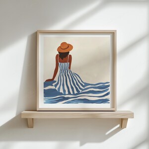 Puede incluir: Impresi&oacute;n art&iacute;stica enmarcada que representa una figura con un vestido a rayas azul y blanco y un sombrero marr&oacute;n, vista desde atr&aacute;s. La obra de arte se exhibe en una estanter&iacute;a de madera contra una pared blanca.