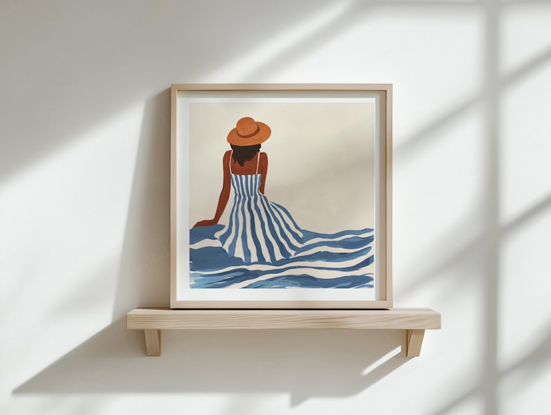 Puede incluir: Impresi&oacute;n art&iacute;stica enmarcada que representa una figura con un vestido a rayas azul y blanco y un sombrero marr&oacute;n, vista desde atr&aacute;s. La obra de arte se exhibe en una estanter&iacute;a de madera contra una pared blanca.