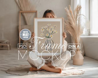 May include: A framed art print mockup featuring a beige background with a vase of daisies. The frame is held by a person. The image includes the text "Frame Mockup" and "With Mat Layer".