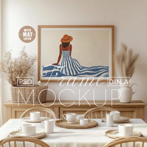 May include: A framed art print depicting a woman in a blue and white striped dress and a brown hat, viewed from the back. The artwork hangs above a wooden cabinet with a woven basket and decorative items. A dining table is set with white crockery.