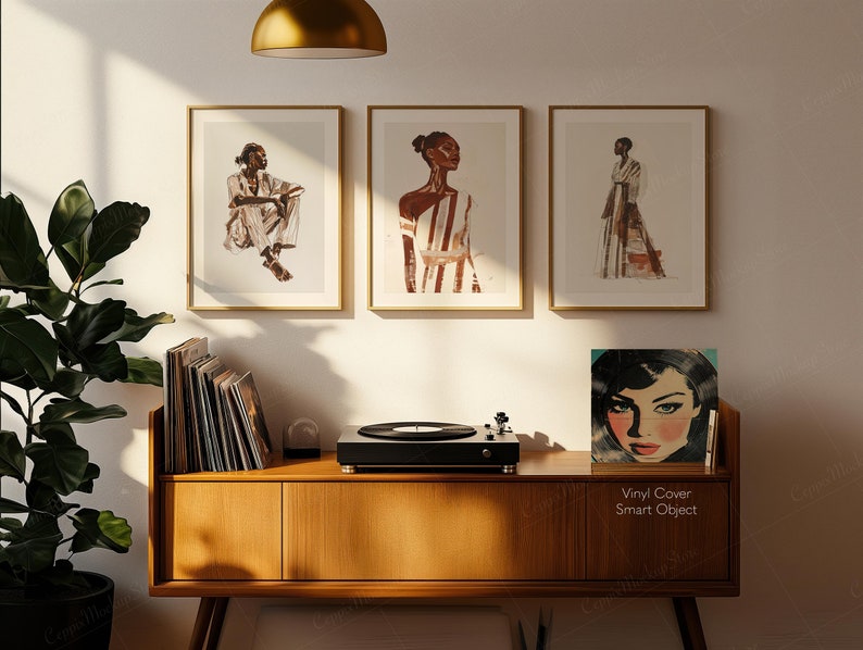 May include: Three framed art prints with gold frames, each featuring a watercolor illustration of a person in fashion. A wooden cabinet holds a record player and vinyl records. A vinyl cover with a woman's face is displayed.